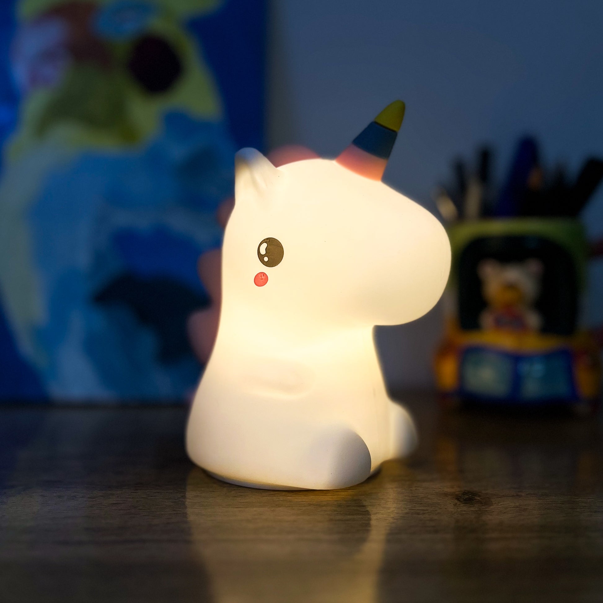 Unicorn-shaped night light on a wooden surface with toys in the background