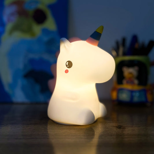 Unicorn-shaped night light on a wooden surface with toys in the background