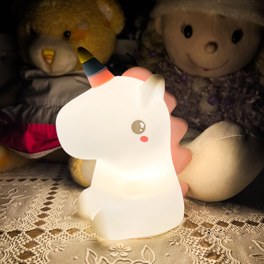 Unicorn-shaped night light held by a hand with teddy bears in the background