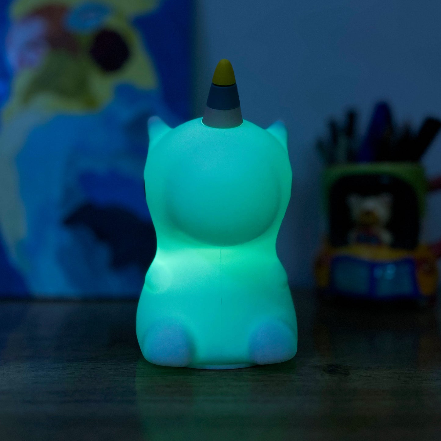 Glowing green Unicorn night light on a dark surface with a blurred colorful background