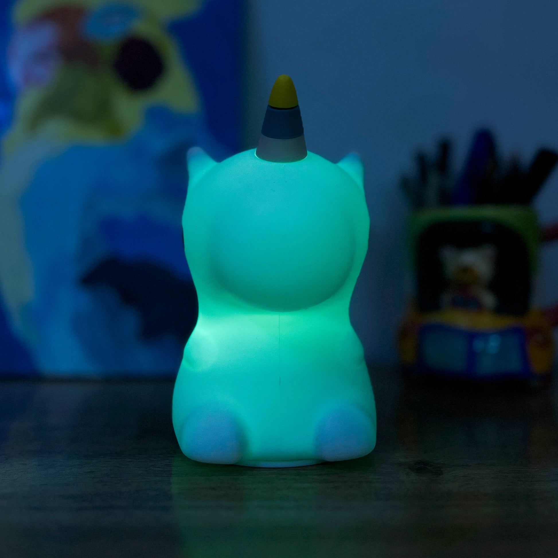 Glowing green Unicorn night light on a dark surface with a blurred colorful background