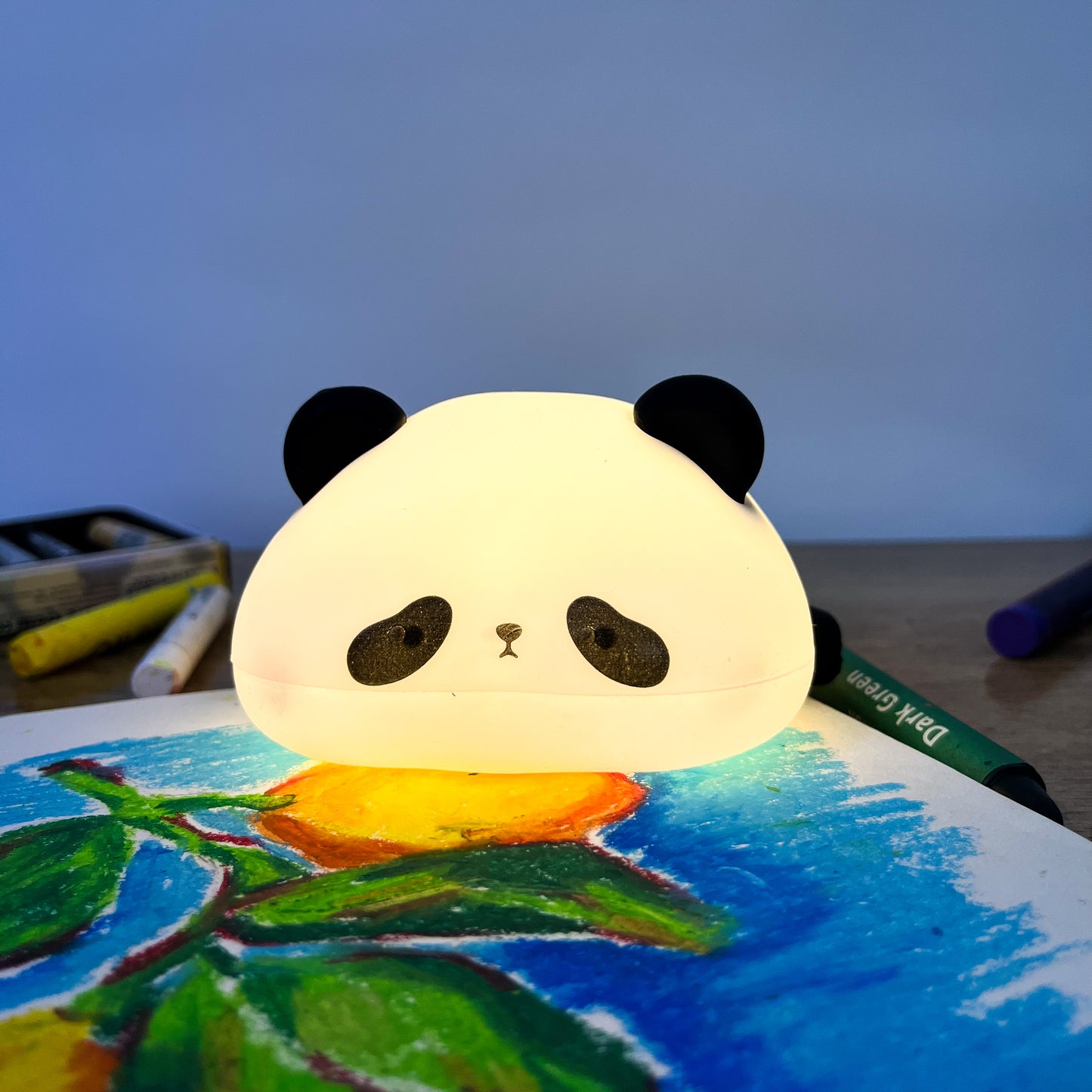 Panda-shaped night light on a child's drawing with art supplies in the background