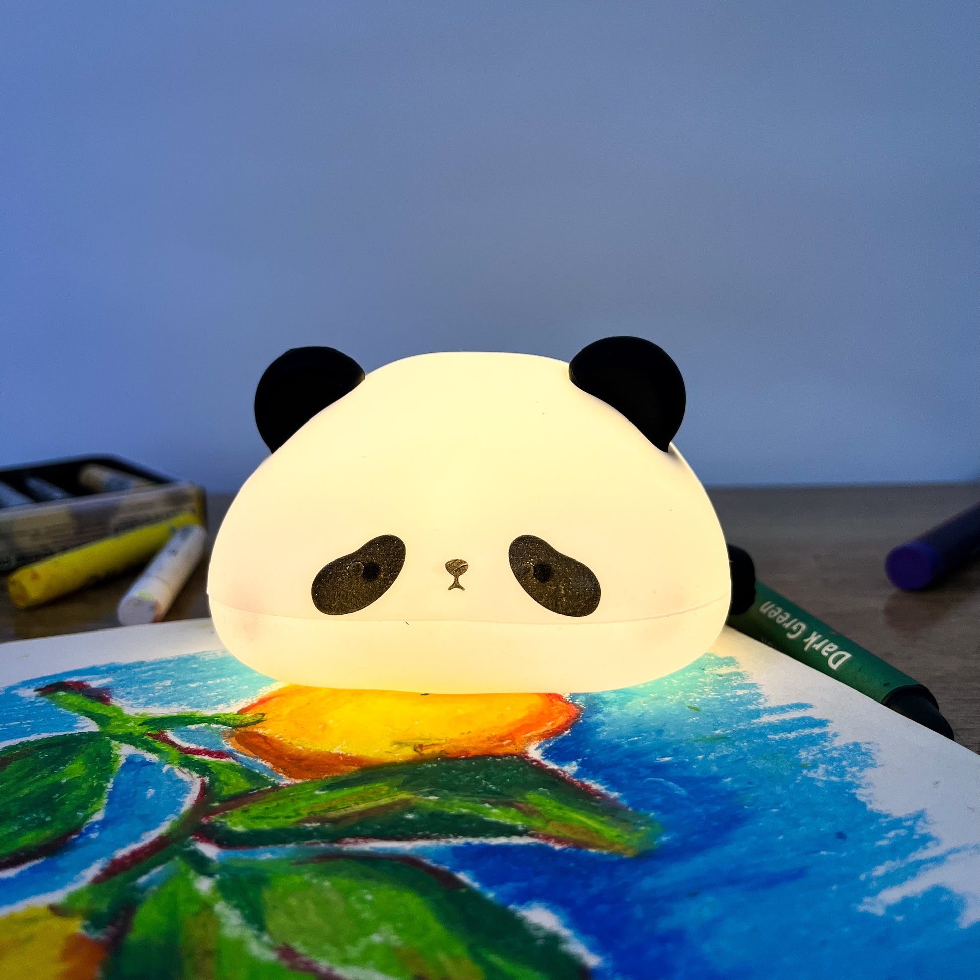 Panda-shaped night light on a child's drawing with art supplies in the background